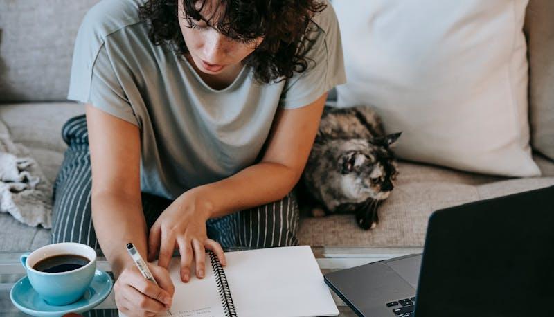 une jeune femme étudie sur un ordinateur avec du café et un chat à côté d'elle